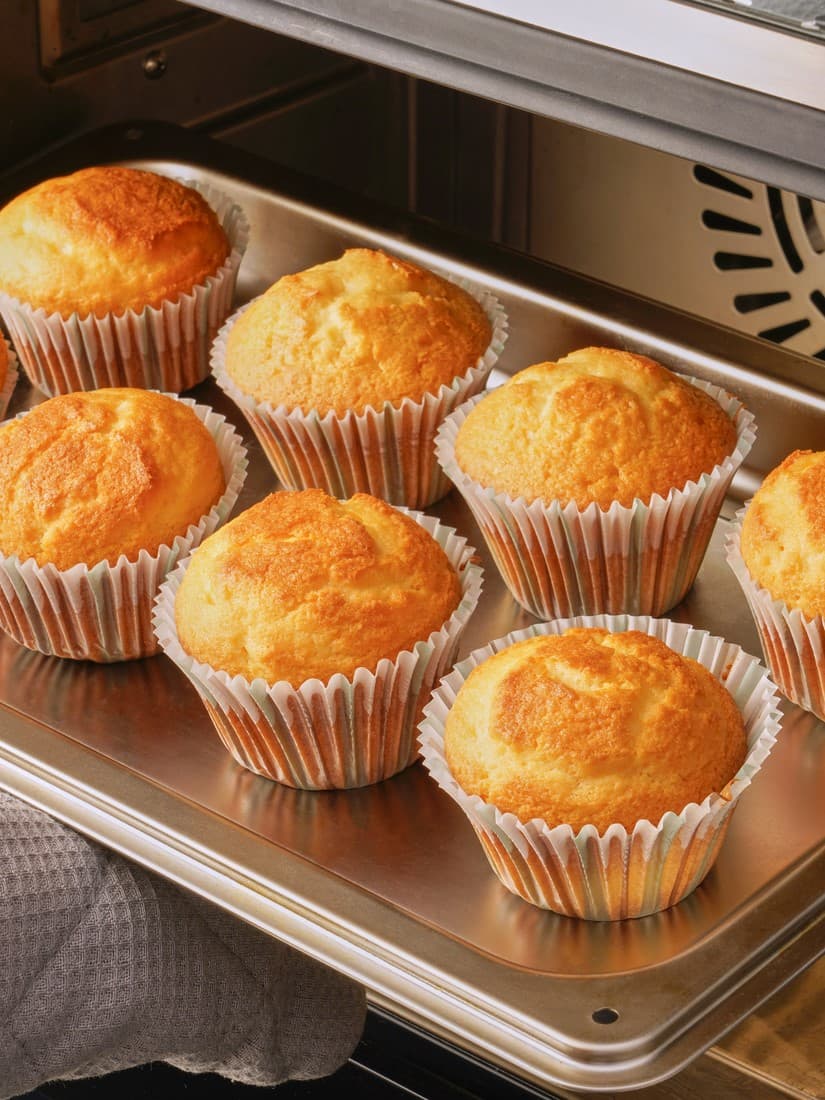 オーブンの中で焼き上がったばかりの、紙カップに入った黄金色のマフィン。