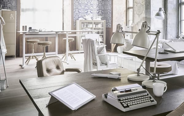 Bureau brun accessoirisé avec une machine à écrire, une tablette et deux lampes de bureau.