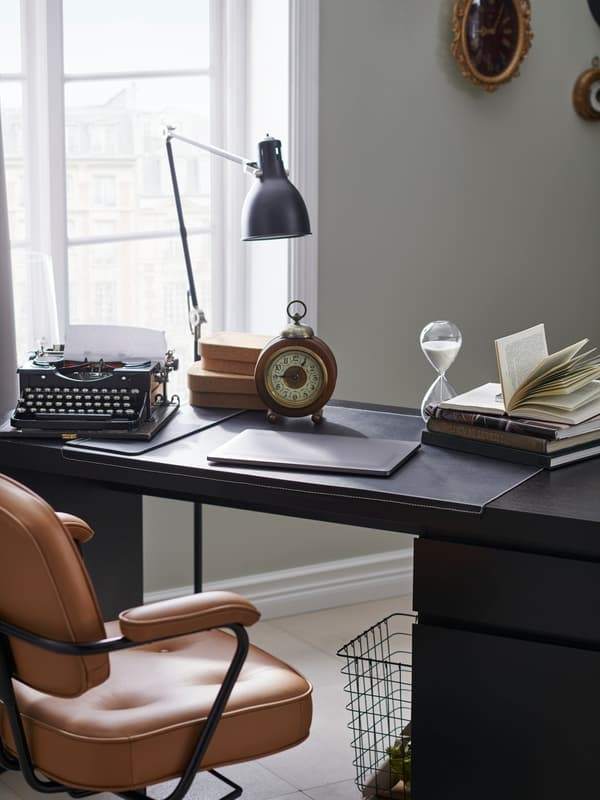 Bureau met leren bureaustoel, laptop, bureaulamp en klok.