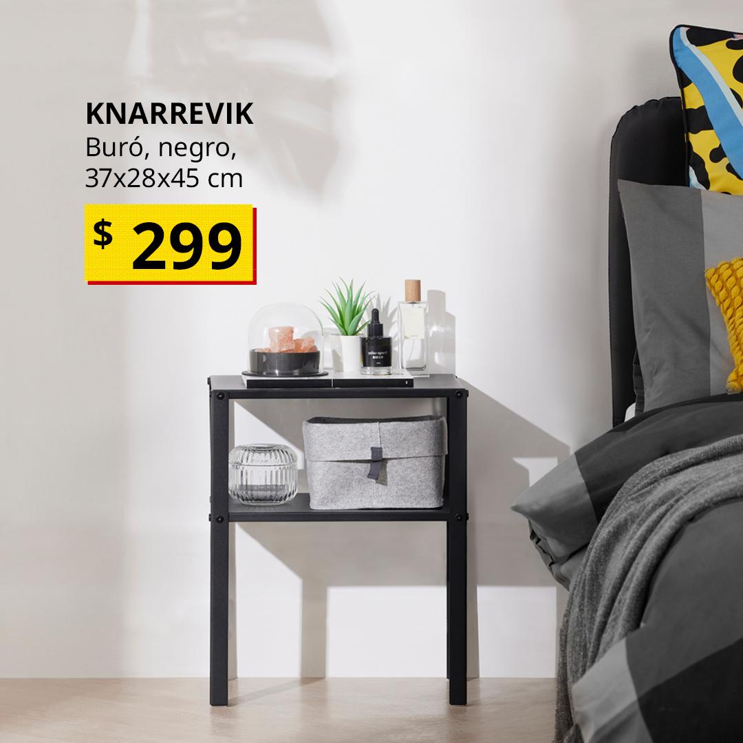 Buró KNARREVIK negro con repisas abiertas junto a una cama, con objetos decorativos y organizadores sobre sus repisas en un dormitorio.