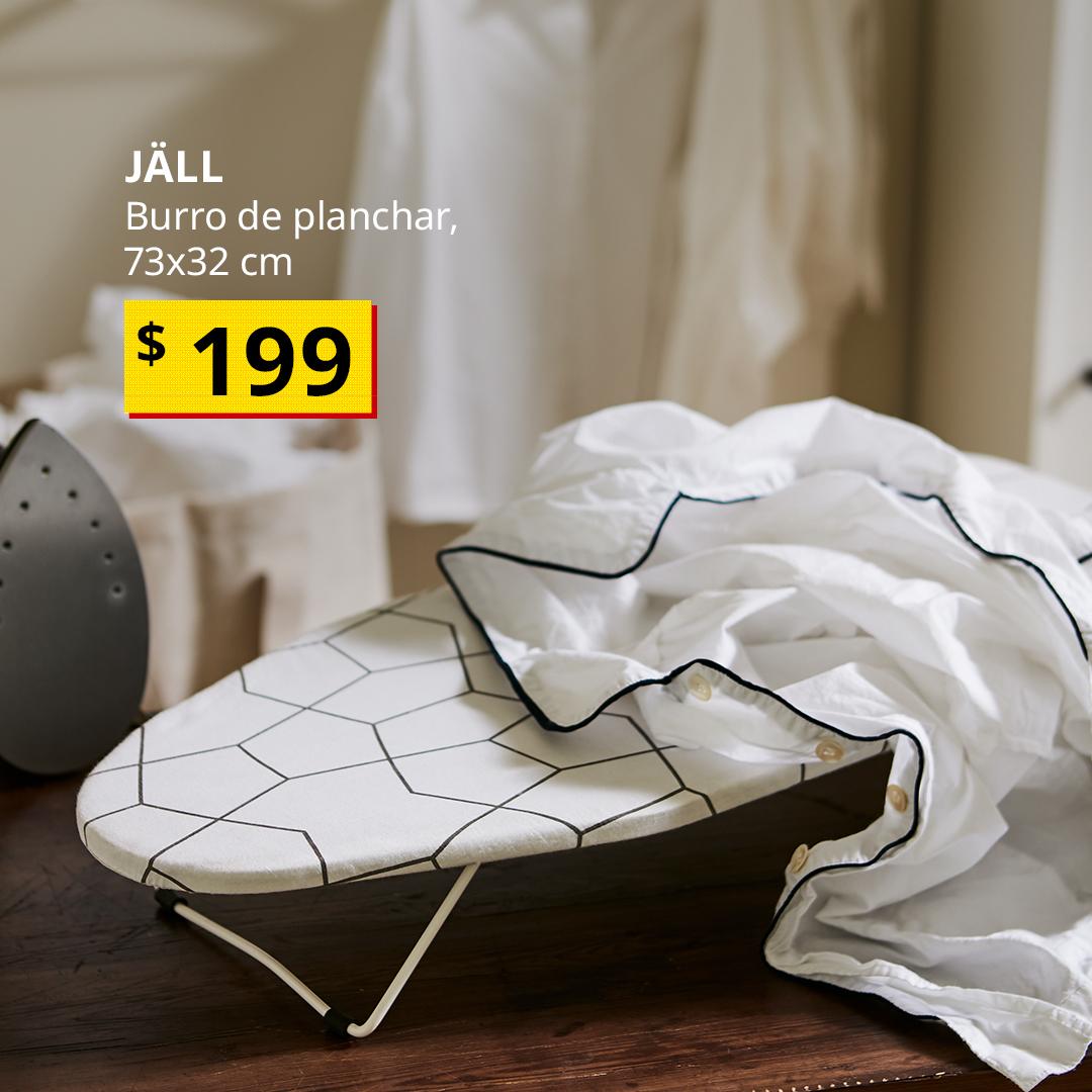 Burro de planchar JÄLL sobre una mesa de madera, junto a una plancha y prendas de ropa en un área de lavado.