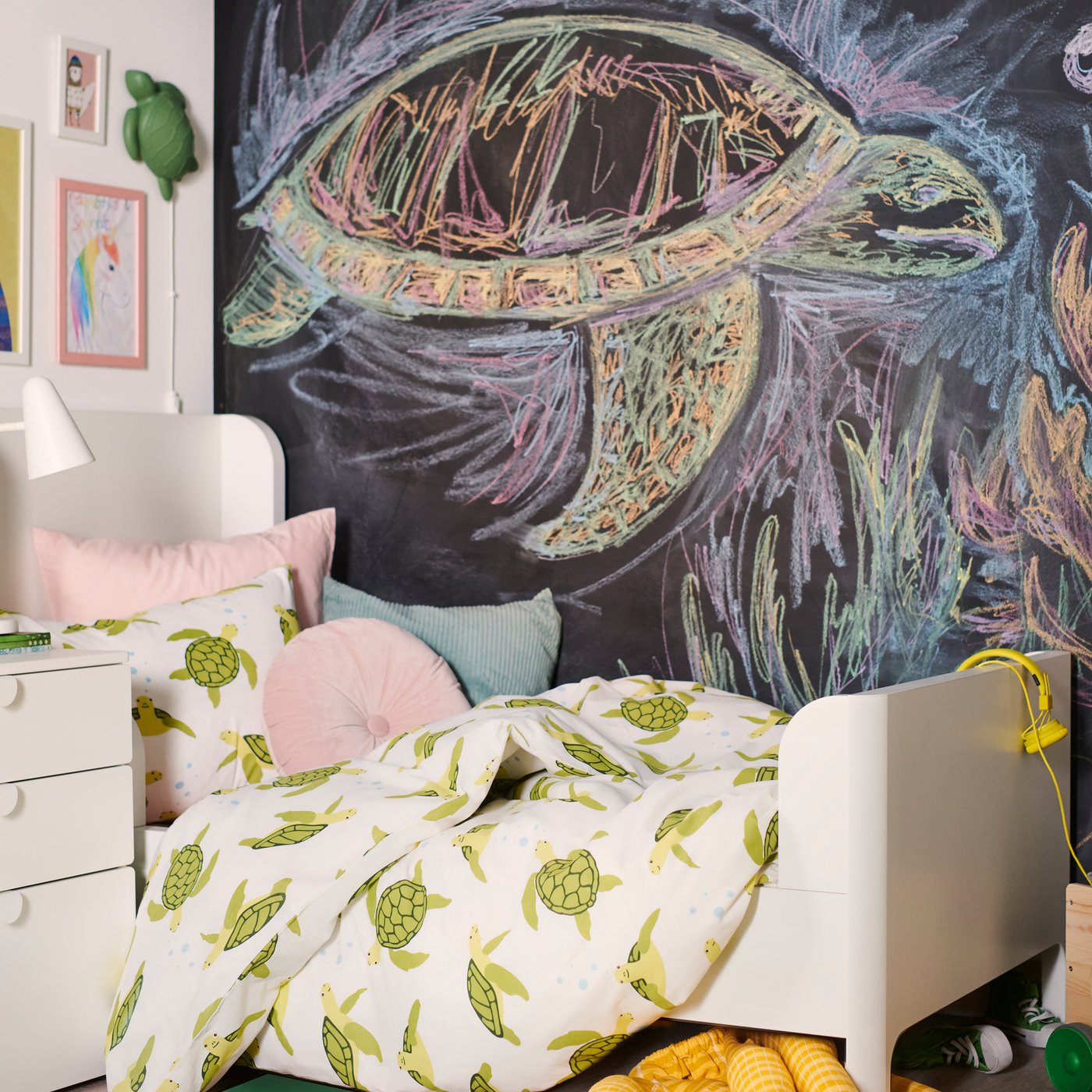 BUSUNGE bed opgemaakt met BLÅVINGAD dekbedovertrek met groene zeeschildpadden en kussens, voor een met bordverf afgewerkte muur.