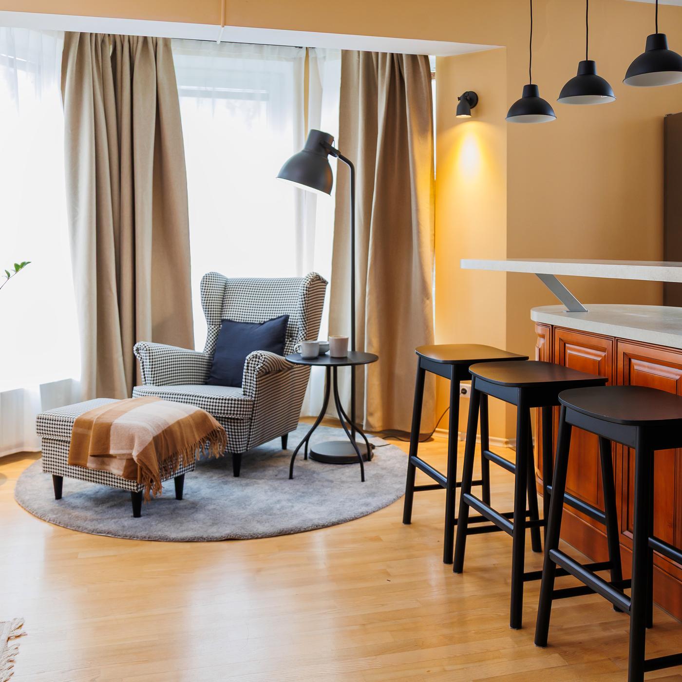 By the living room window, on a round grey rug, stands a STRANDMON armchair with a matching footstool.