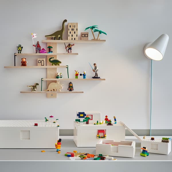 BYGGLEK 뷔글레크 LEGO® 블록과 상자가 놓여 있는 화이트 색상의 테이블. 뒤의 벽에는 화이트 전등과 장난감이 놓인 선반이 보입니다.