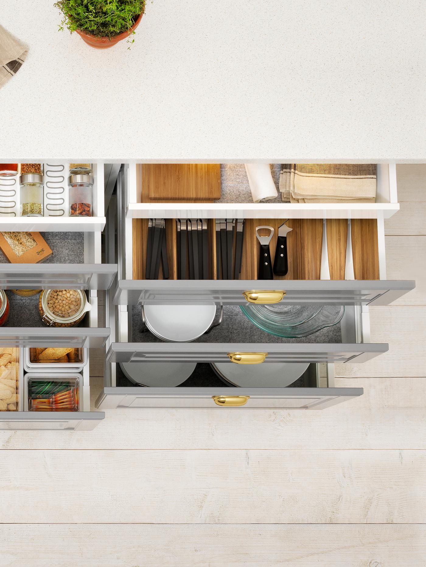 Cabinets with grey drawer fronts where all the drawers are open, containing dry goods, cutlery, cookware and tableware.