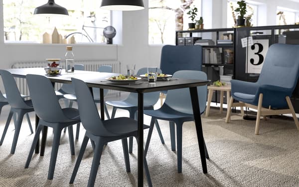 Cadeiras IKEA ODGER con forma redondeada en negro e mesa de comedor rectangular LISABO negra nunha área de planta aberta para comer.