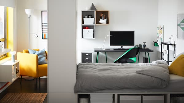 Cadre de lit PLATSA avec rangement dans une pièce avec fauteuil et chaise pivotante verte devant un bureau monté sur des tréteaux verts.