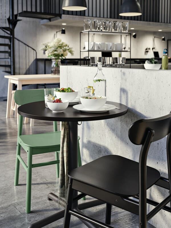 Café-Einrichtung mit einem grünen und einem schwarzen Stuhl sowie einem schwarzen Rundtisch.