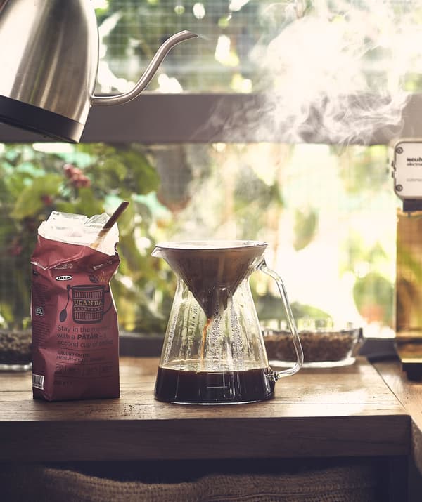 Café facéndose cun xardín de fondo; auga quente da fervedoira filtrándose a unha xarra de vidro.