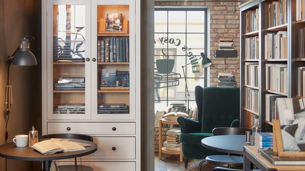 Café with café furniture and large displays of books in bookcases, spotlights and an armchair in dark green velvet.