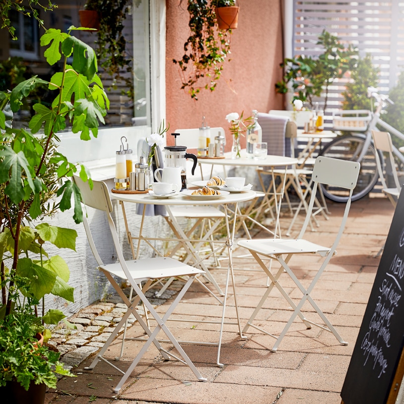 Caffè all’aperto con tavoli e sedie da giardino TUNHOLMEN in grigio. Diversi tavoli e sedie sono impilati o ripiegati – IKEA
