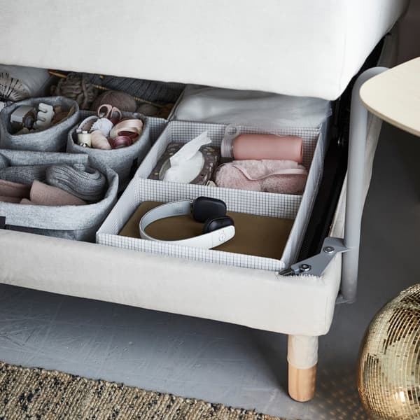 Caixas de almacenaxe IKEA STUK cheas de accesorios, mostradas debaixo do sofá cama.