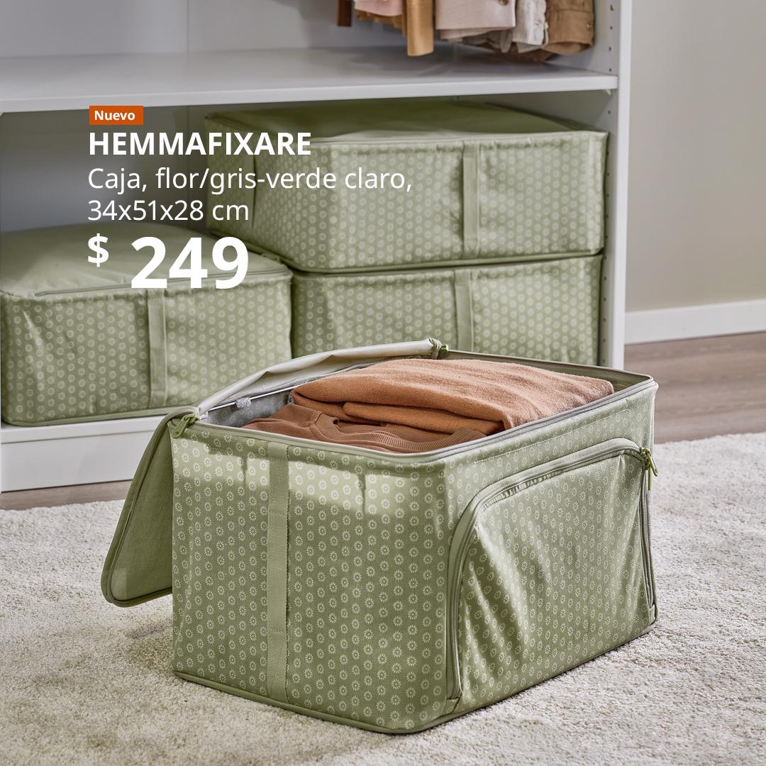 Caja de almacenamiento HEMMAFIXARE color verde claro con estampado floral, abierta y llena de ropa doblada, frente a un armario.