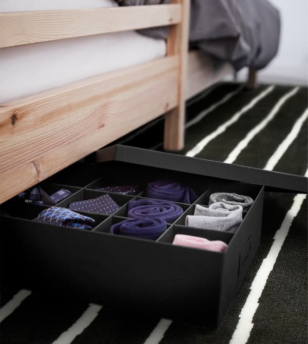 Caja TJENA con compartimentos debajo de una cama, con calcetines y pequeños accesorios.