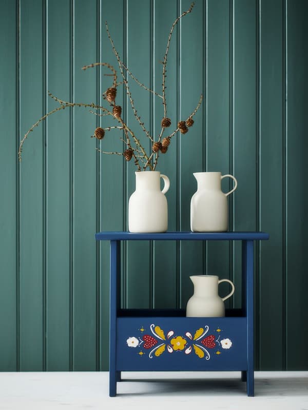 Cajón de madera azul con motivos de flores y con tres jarones blancos. 