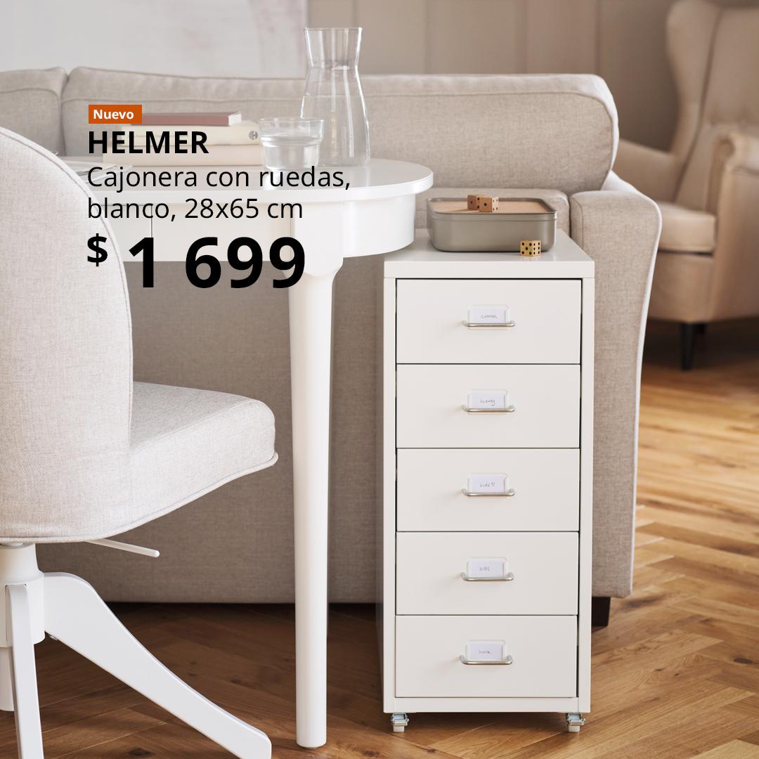 Cajonera HELMER blanca con ruedas junto a un escritorio ROSENTORP blanco, ubicado detrás de un sofá.