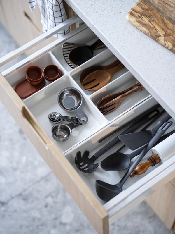 Cajones organizadores UPPDATERA blancos en el interior de cocina. Están con utensilios de cocina como cubiertos, medidores, cubiertos de madera y más.