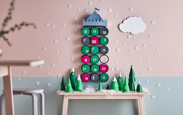 Calendrier de l'Avent avec sapins en papier posés sur une table et château accroché au mur.