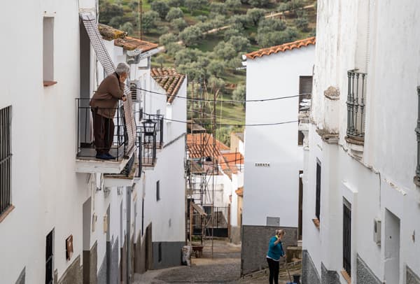 Calle de pueblo andaluz con casas blancas y señora asomada al balcón.