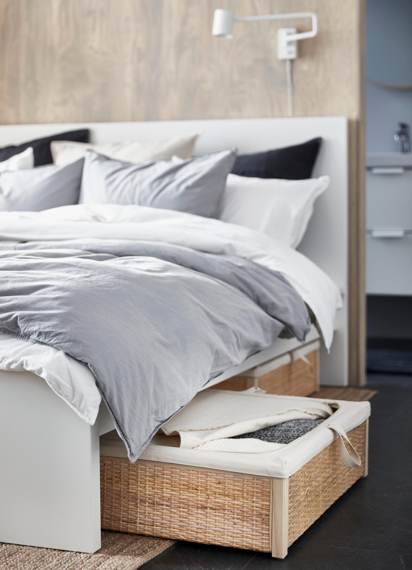 Cama blanca MALM con ropa de cama gris, cojines blancos y oscuros ÄNGSLILJA. La cama tiene cajones para almacenar cosas en su parte inferior.