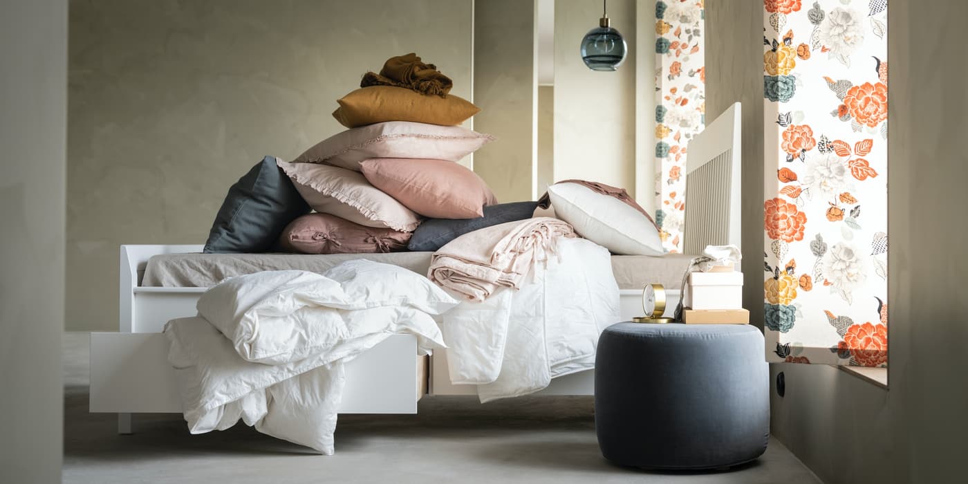 Cama blanca MALM cona almacenamiento, cubierta con ropa de cama y cojines de distintos colores.