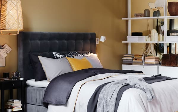 Cama con cabeceiro tapizado en veludo gris e roupa de cama superposta.