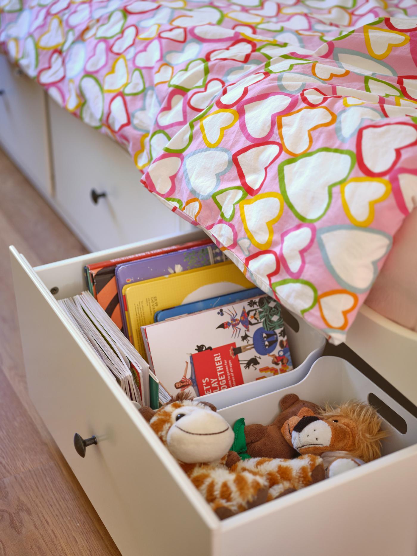 Cama de niña o cama infantil con cajones blancos VARIERA en la parte inferior, donde hay libros y peluches guardados.