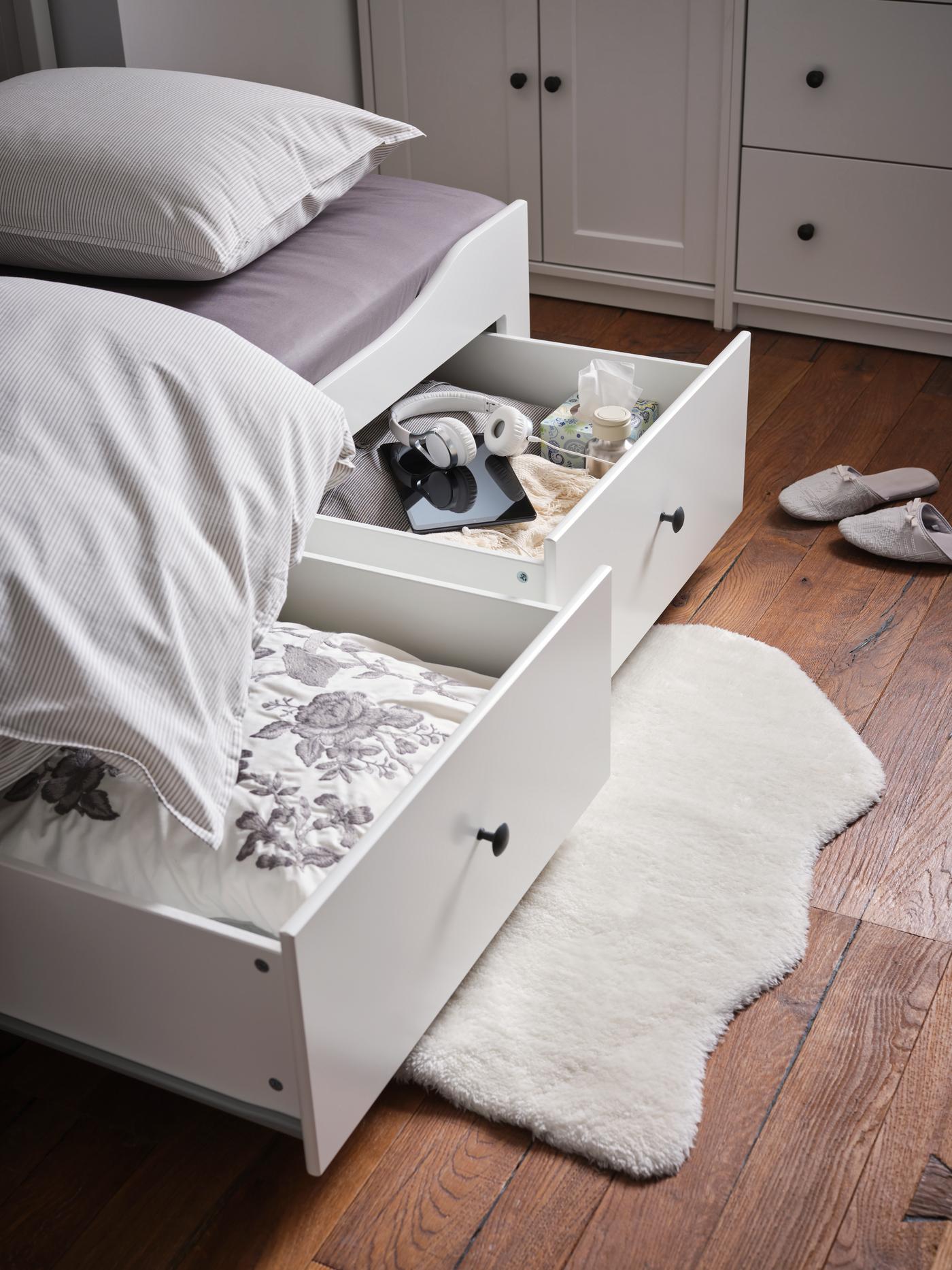 Cama HEMNES con cajones blancos sobre una alfombra de piel blanca en un piso de madera.
