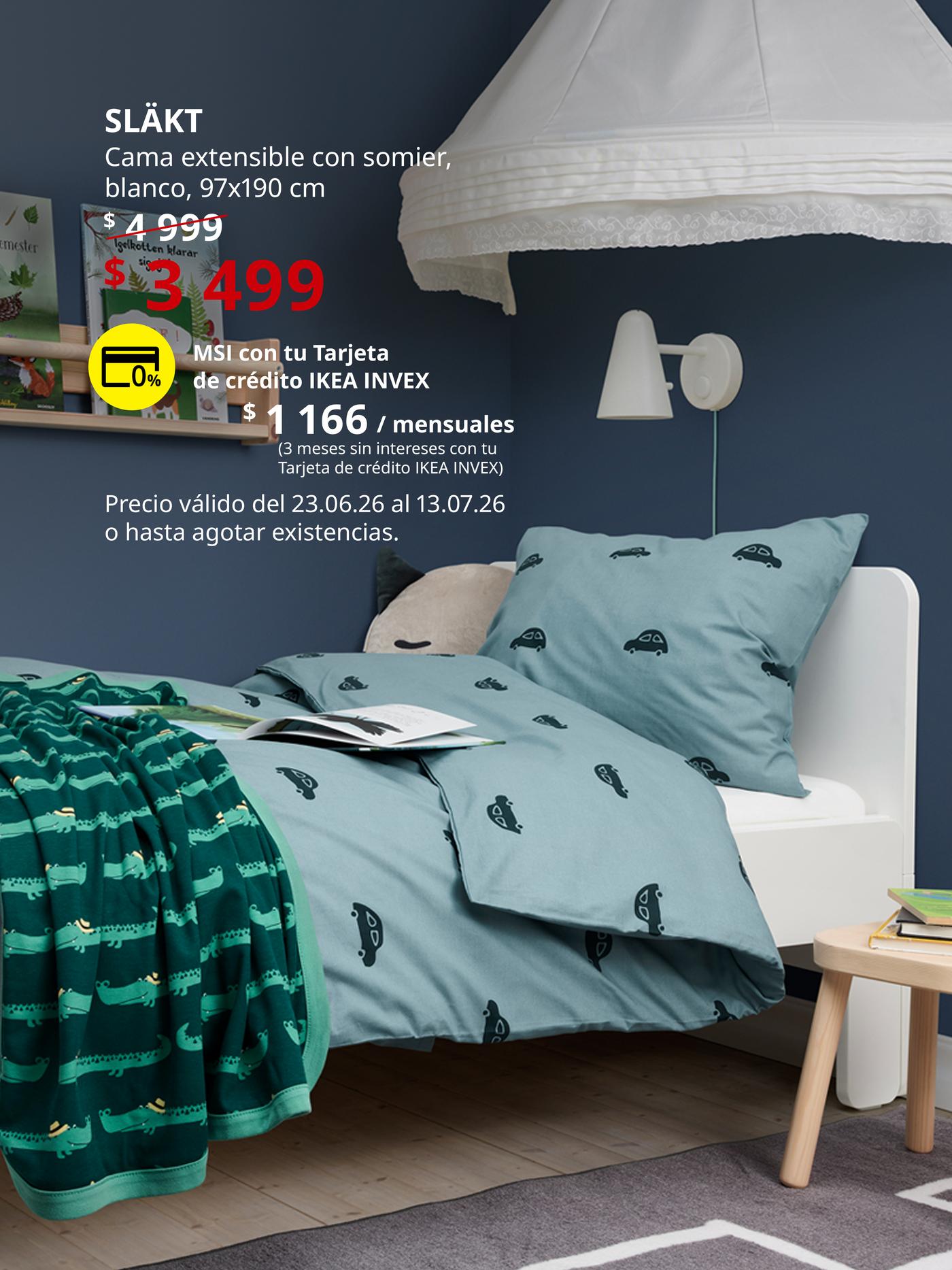 Cama infantil SLÄKT blanca en habitación infantil con ropa de cama estampada, lámpara de pared y mesita auxiliar.