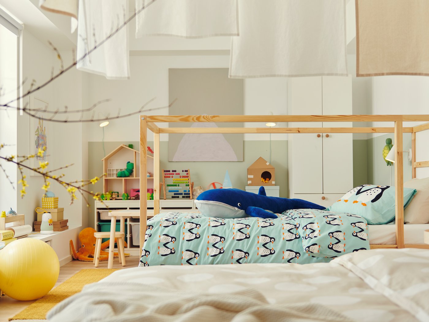 Cama KURA de madeira no centro de quarto de criança grande. Em cima do edredão, baleia de peluche gigante.