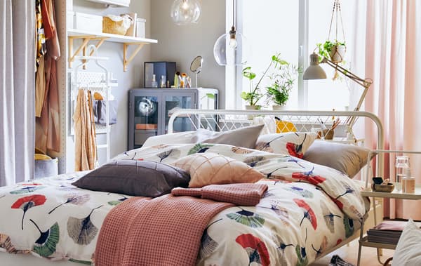Cama vestida con roupa de estampado floral no centro dun cuarto con almacenamento e estantes nas paredes.