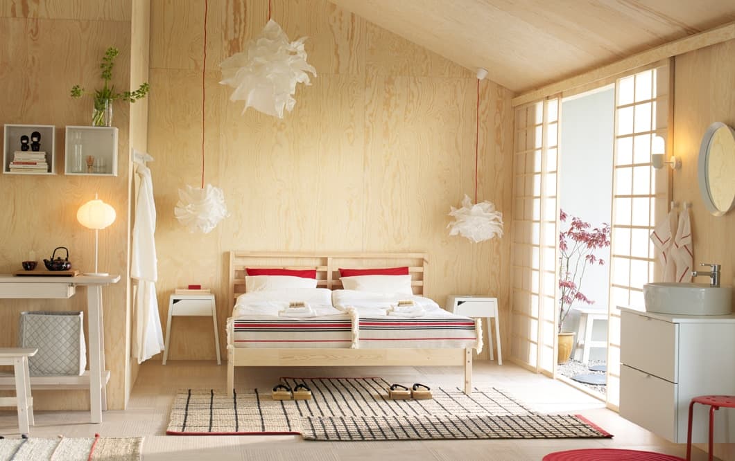 Camera con letto matrimoniale in pino massiccio grezzo, biancheria da letto bianca e rossa, e comodini bianchi – IKEA