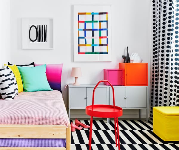 Camera da letto arredata in stile color block e motivi grafici con un letto ricoperto di cuscini accanto a dei mobili EKET.