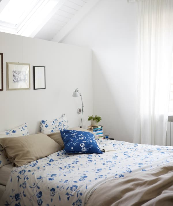 Camera da letto bianca con copripiumino floreale bianco e blu sotto un lucernario.