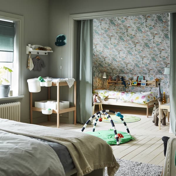 Camera da letto con letto matrimoniale, fasciatoio e accessori per un neonato. In una nicchia dietro tende verdi c’è un lettino.