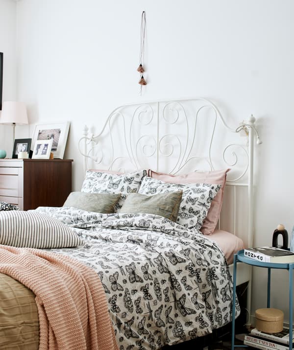 Camera da letto con un letto bianco dalla struttura in ferro battuto e lenzuola con fantasia a farfalle e coperte rosa, accanto una cassettiera in legno scuro - IKEA