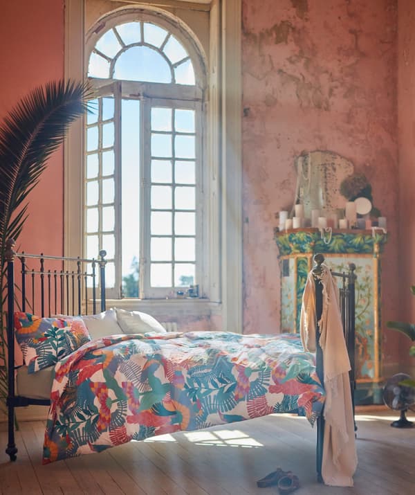 Camera da letto con un'ampia finestra ad arco illuminata dal sole. Letto in metallo con biancheria SKOGSFIBBLA.