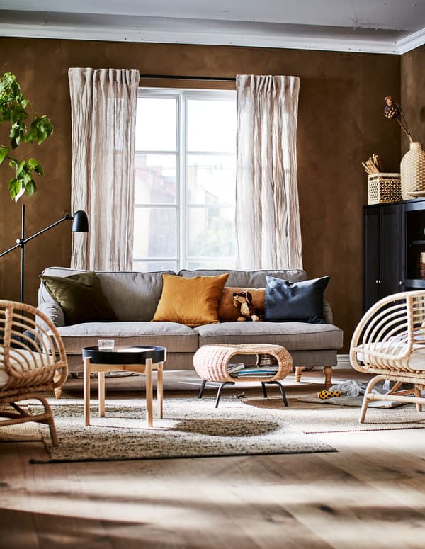 Cameră de zi cu schemă cromatică în culorile pământului, cu decorațiuni, corpuri de depozitare, scaune, măsuță de cafea, un taburet cu spațiu de depozitare și o plantă.