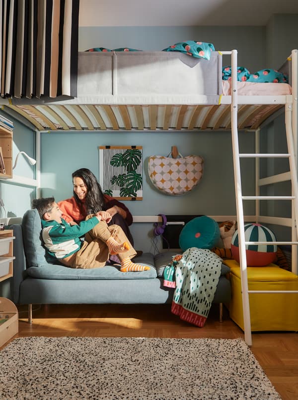 Cameretta con una mamma e un bambino seduti in un confortevole angolo relax, creato sotto un letto a soppalco VITVAL bianco.