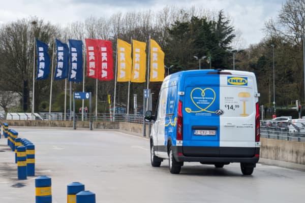 Camionnette de livraison IKEA dans un parking avec des drapeaux IKEA visibles en arrière-plan.