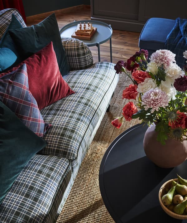 Canapé à motif tartan et coussins colorés, tables d’appoint et vase garni de fleurs, vus d’en haut.