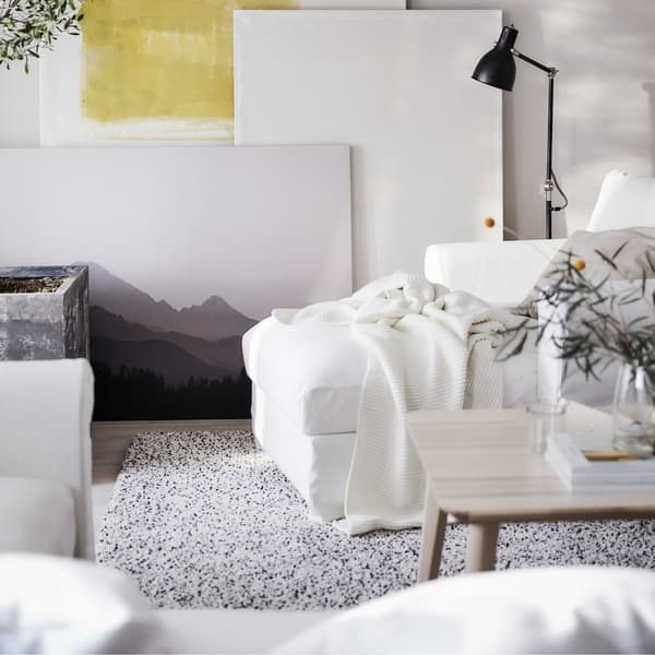 Canapé d’angle HÄRLANDA houssé en blanc, grande plante, et coussins et jetés de tons neutres dans un salon lumineux.