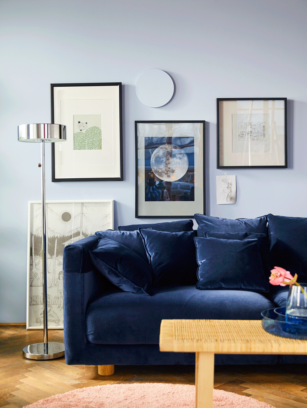 Canapé en velours bleu avec affiches tropicales sur le mur du fond. GIF montrant de nouveaux coussins dans des couleurs claires ajoutés à un canapé.
