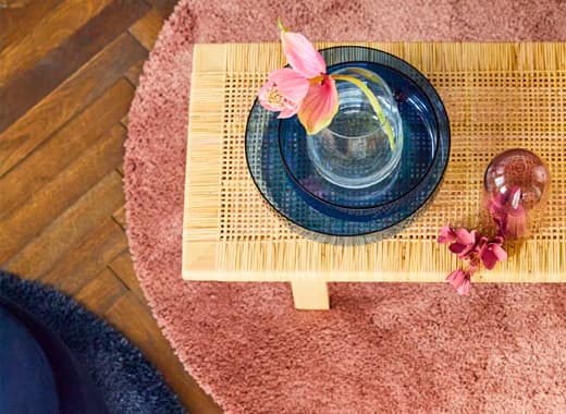 Canapé en velours bleu avec pouf assorti placé devant et lampadaire rond métallique placé à côté, plus des vases en verre colorés de forme arrondie posés sur une table basse, le tout de chez IKEA.