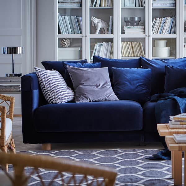 Canapea STOCKHOLM 2017 din catifea albastru închis, cu perne împrăștiate, pe un covor albastru cu model, într-un decor de cameră de zi.