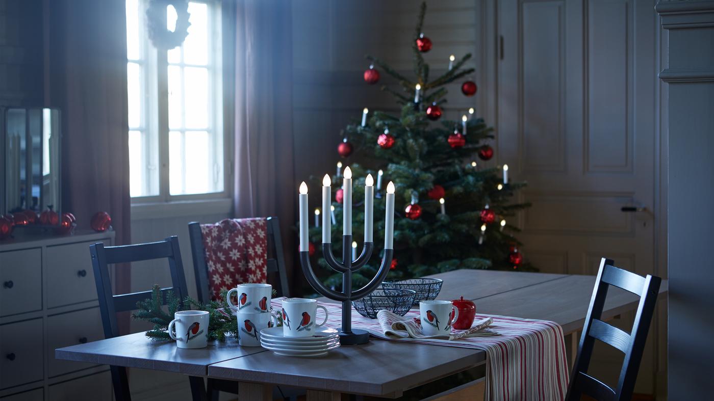 Candelabro a LED STRÅLA a 5 bracci nero su un tavolo, in una cucina illuminata da una luce soffusa, con un albero di Natale sullo sfondo.