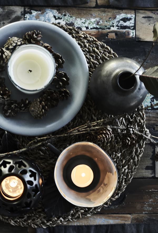 Candles and pine cones displayed on a woven placemat.