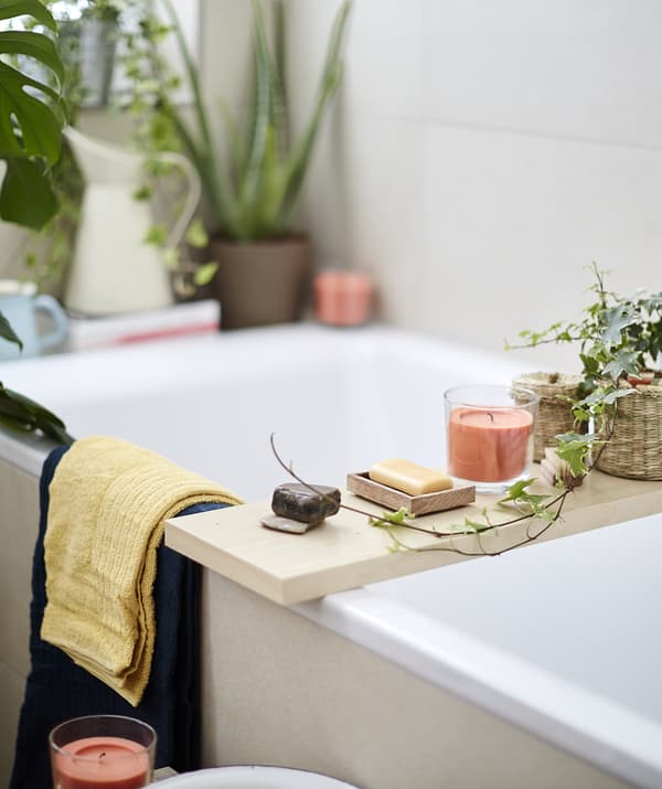 Candles, soap and plants on a wooden board laid across a bath.