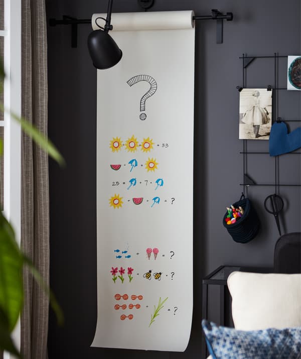 Canto de uma sala com um rolo de papel para desenhar pendurado na parede, com problemas de matemática coloridos desenhados na folha.