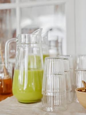 Carafe avec un jus vert à côté de verres empilés